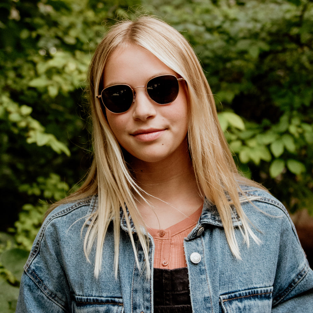 Girl wearing gold round sunglasses and a blue shirt 